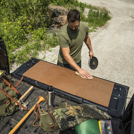 Man cleaning a Epicurean cutting board on the back of a truck, surrounded by nature.