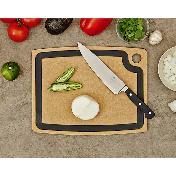 Epicurean gourmet series chopping board with knife, vegetables, and a kitchen towel on a countertop