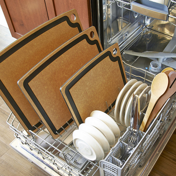 Open dishwasher with natural Epicurean gourmet series cutting boards, white plates, and wooden spoons.
