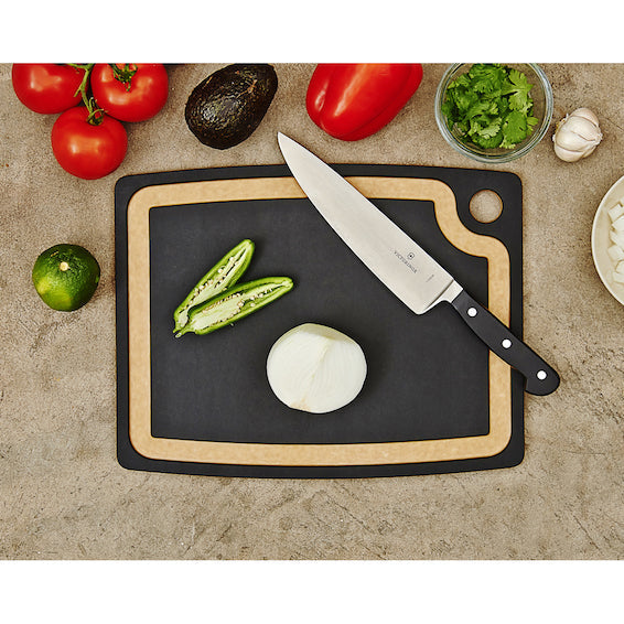 Knife on a Epicurean gourmet cutting board with juice groove and vegetables on a stone surface