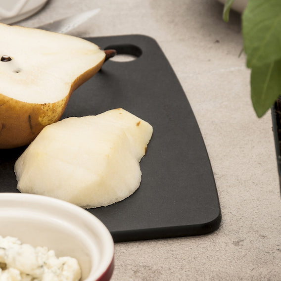 Two pears on a Epicurean kitchen series black cutting board with a bowl of crumbled cheese on a light gray surface.