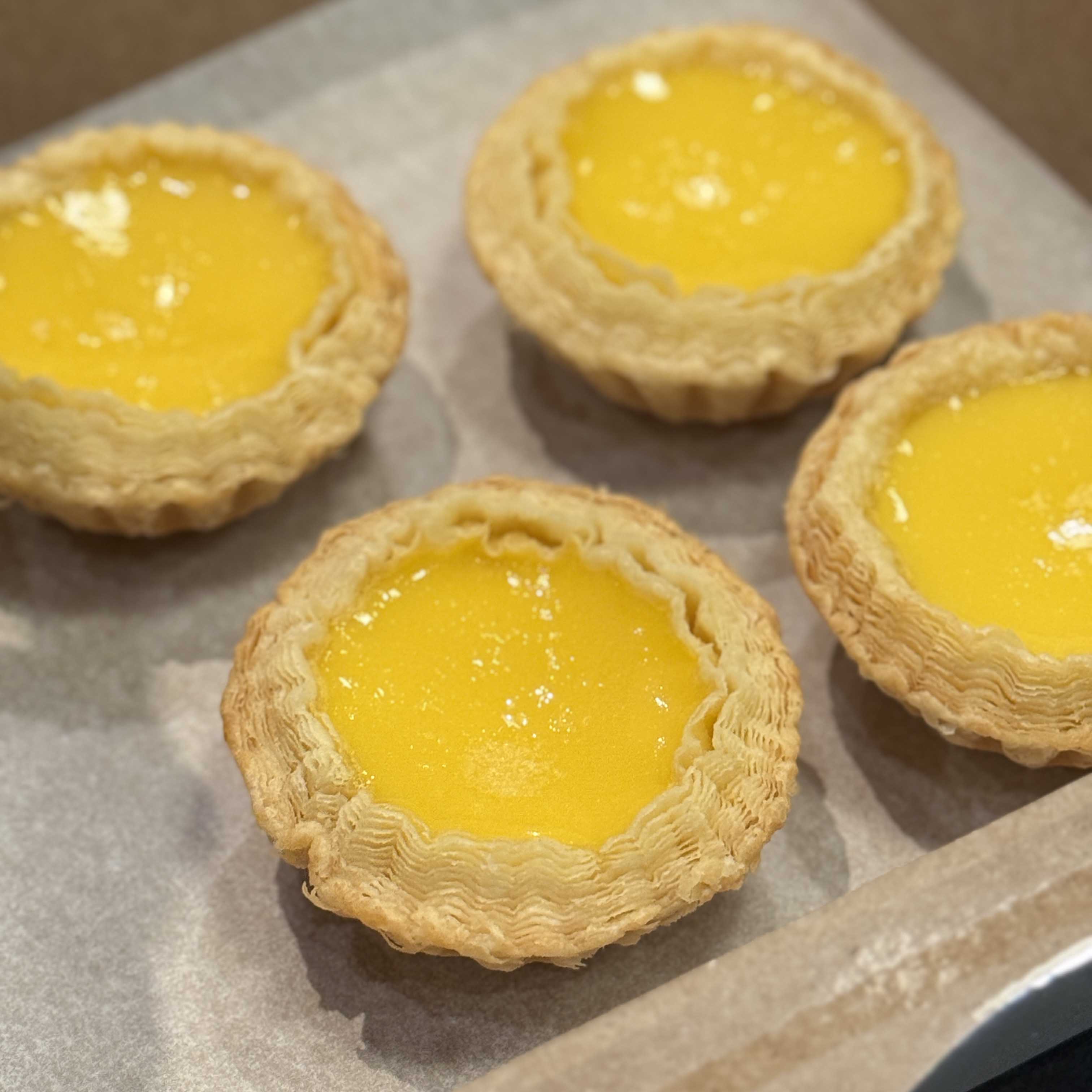 Four yellow Hong Kong egg tarts on a baking tray