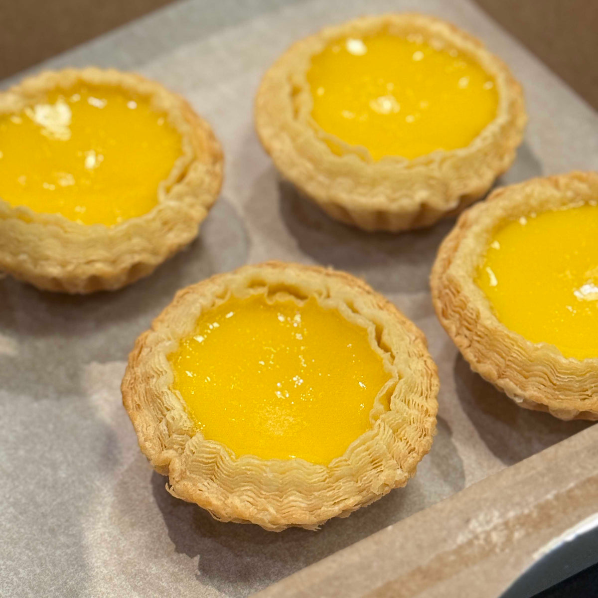 Four yellow Hong Kong egg tarts on a baking tray