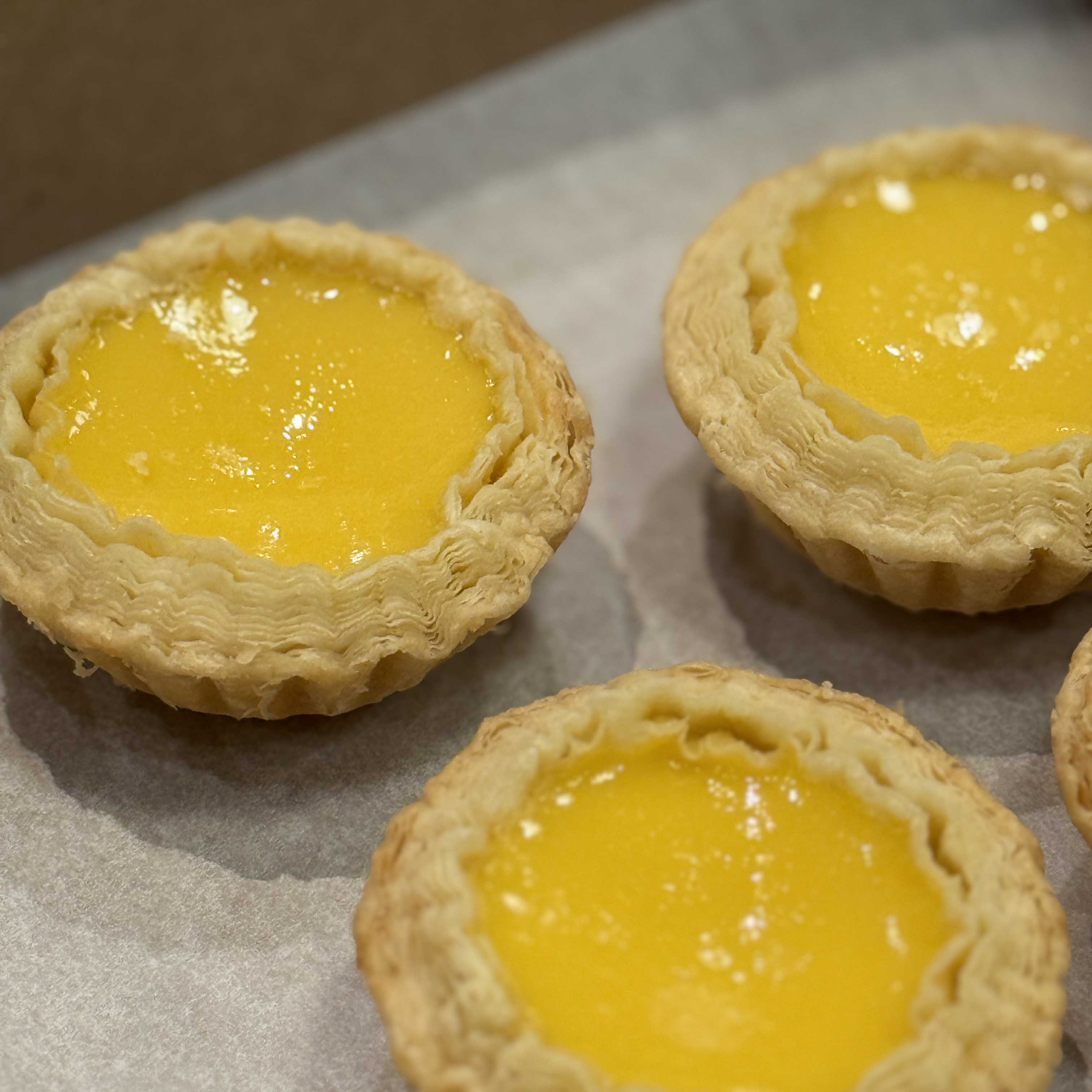 Three yellow Hong Kong egg tarts on a baking sheet