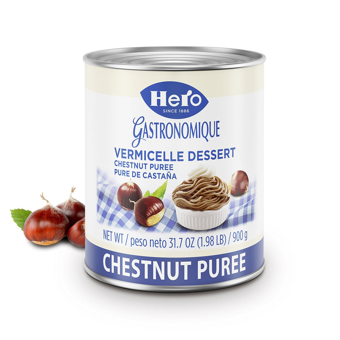 A can of Hero Gastronomique Chestnut Puree dessert, shown on a clean white background with a few whole chestnuts and a leaf as styling props. The can features a white label with blue branding and illustrations of the product.
