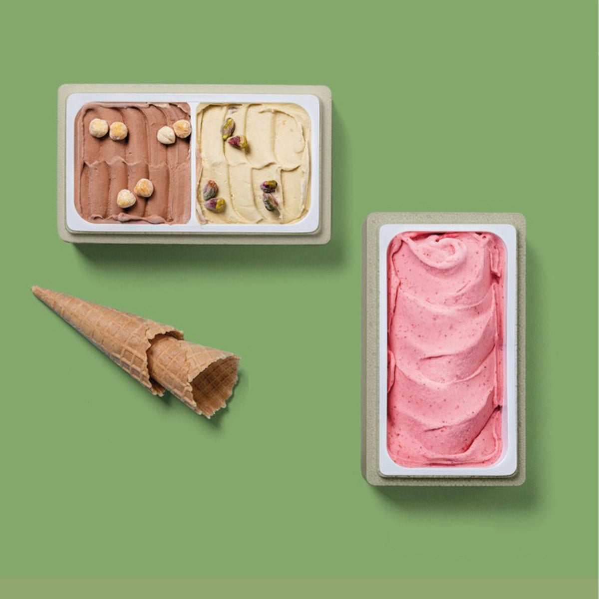 Two open ice cream containers and a waffle cone on a solid sage green background. The left container holds two scoops: one chocolate brown with hazelnuts and one creamy beige with nuts.