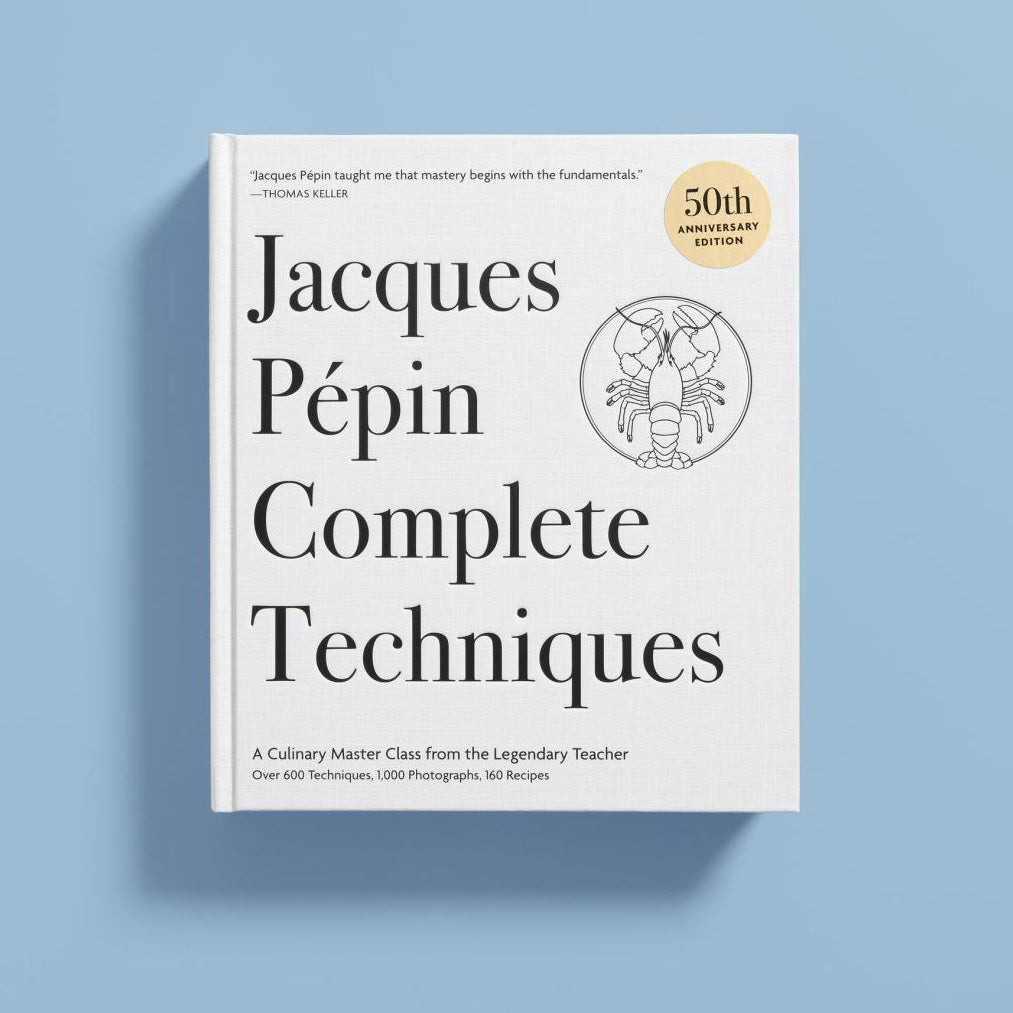 The front cover of the book 'Jacques Pépin Complete Techniques' is shown standing upright against a light blue background. The cover is white with large black typography and a small gold '50th Anniversary Edition' seal near the top right.