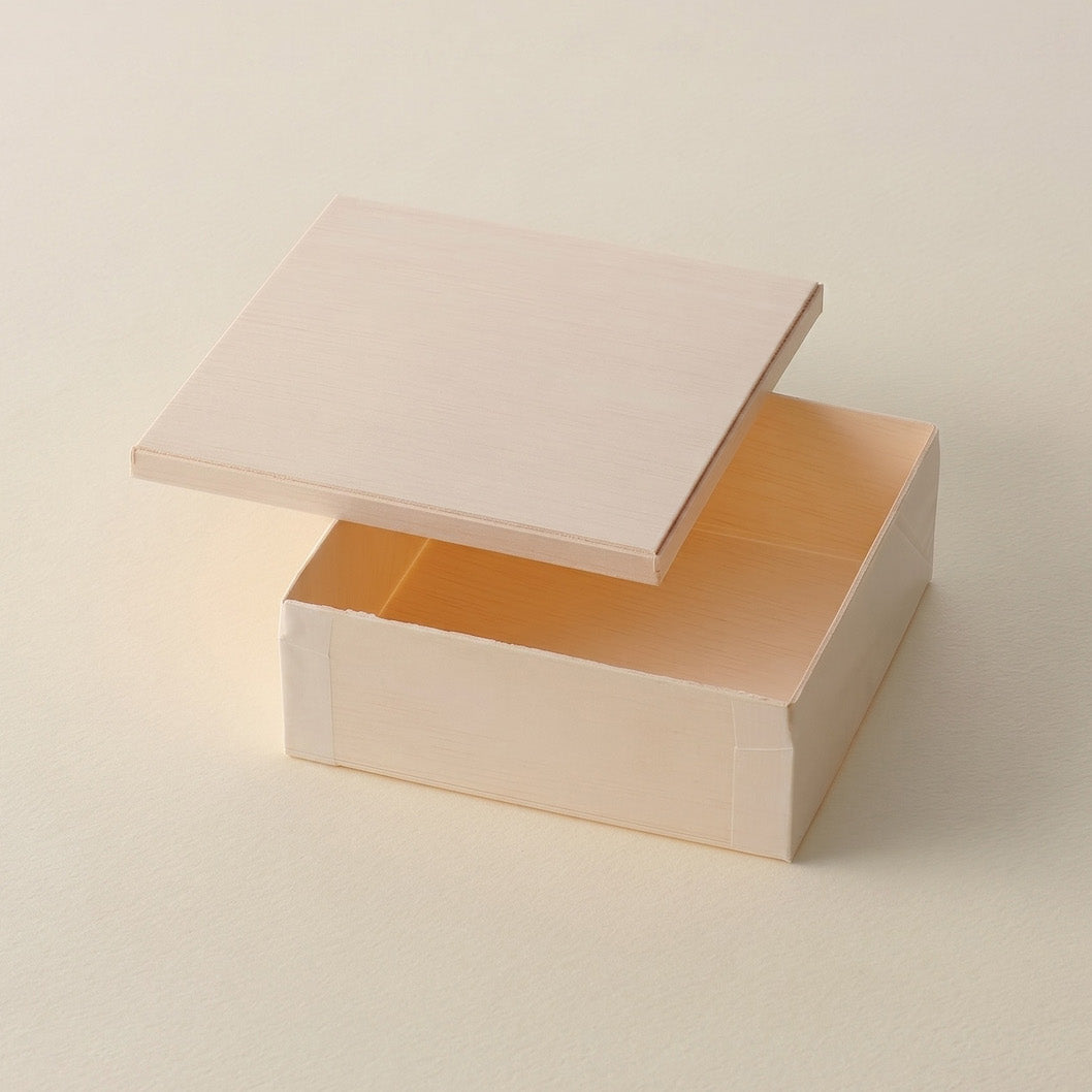 A small square cardboard box with its lid slightly offset, showing a warm beige exterior and a peachy-orange interior, set against a matching light beige background.