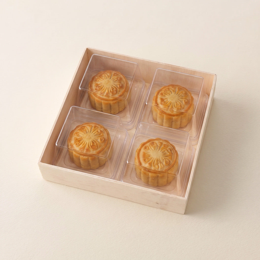 Four golden-brown mooncakes in clear plastic individual compartments inside a light beige wooden gift box, photographed on a clean off-white background.