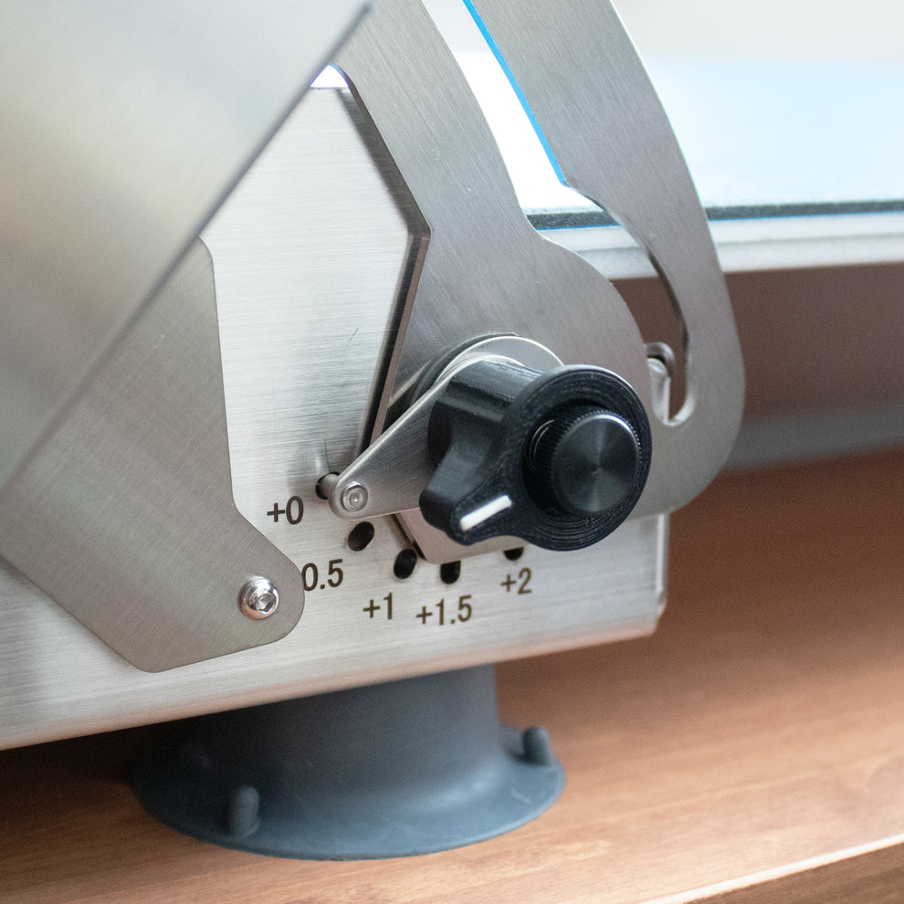Close-up of a dough sheeter with a knob and measurement markings on a wooden surface.