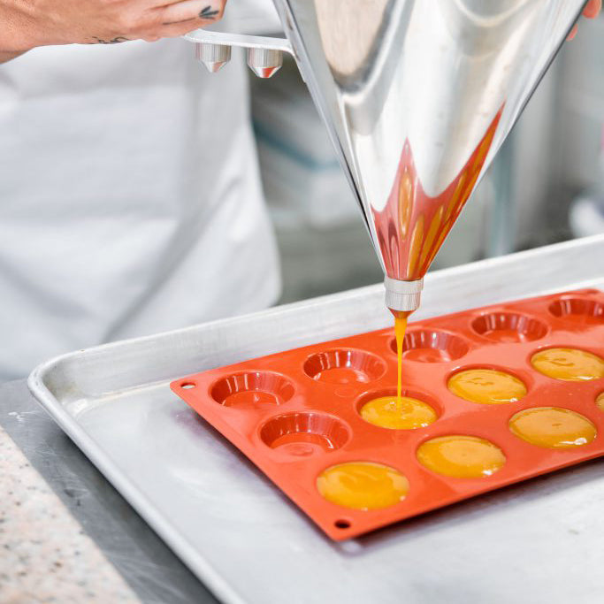 Silicone mold being filled with yellow batter using a metal funnel.