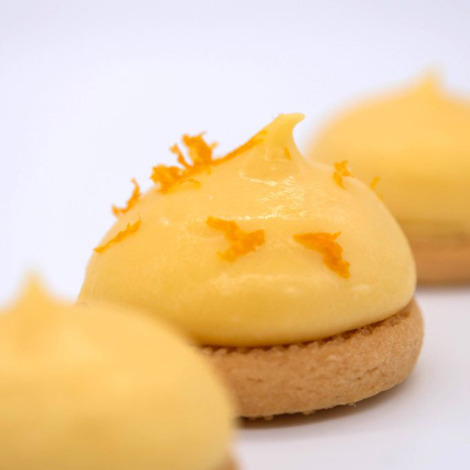 Close-up of a dessert with yellow cream and orange zest on a white background