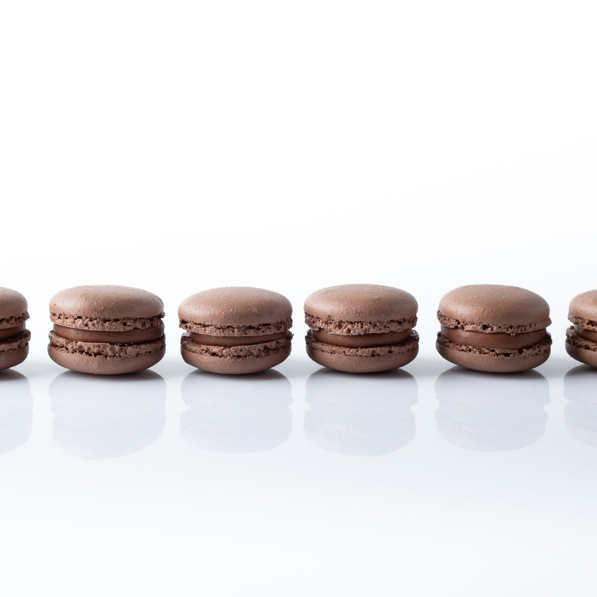 Chocolate macarons arranged in a row on a white surface