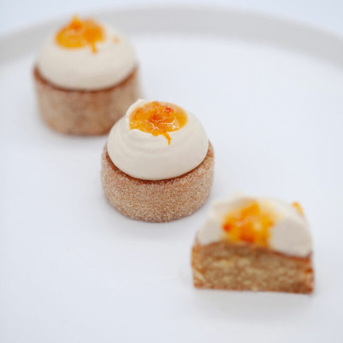 Three small dessert bites with white cream and orange zest on a white plate