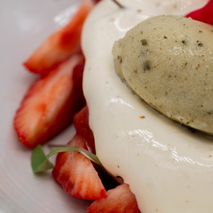 Close-up of a mousse dessert, white cream, and strawberries on a white plate.