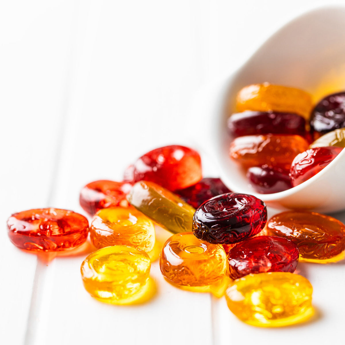 Colorful gummy candies with a white bowl containing more candies on a white background
