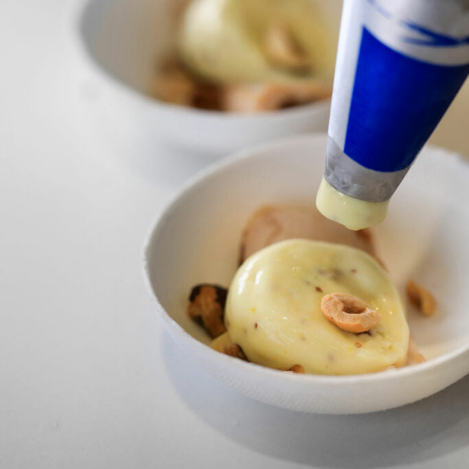 Cream being pipped with a blue and white tube on a white bowl.