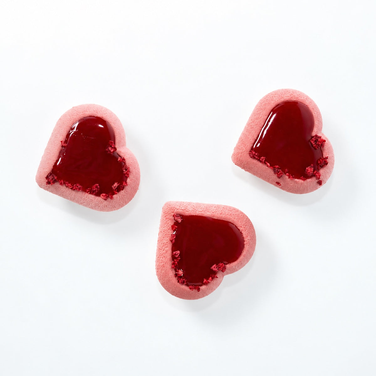 Three heart-shaped pink pastries with glossy dark red centers and glittery red edges, arranged on a clean white background.
