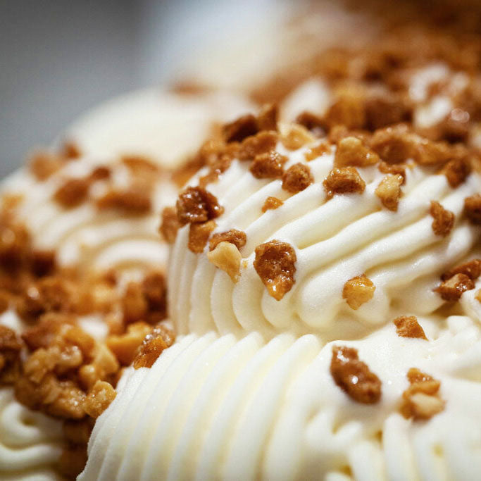 Close-up of a whipped cream or frosting surface with piped swirls and scattered chopped brown nuts or caramelized topping.