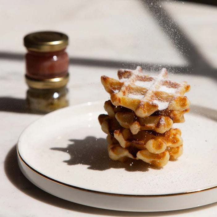 Stack of waffles on a plate with a jar of syrup in the background