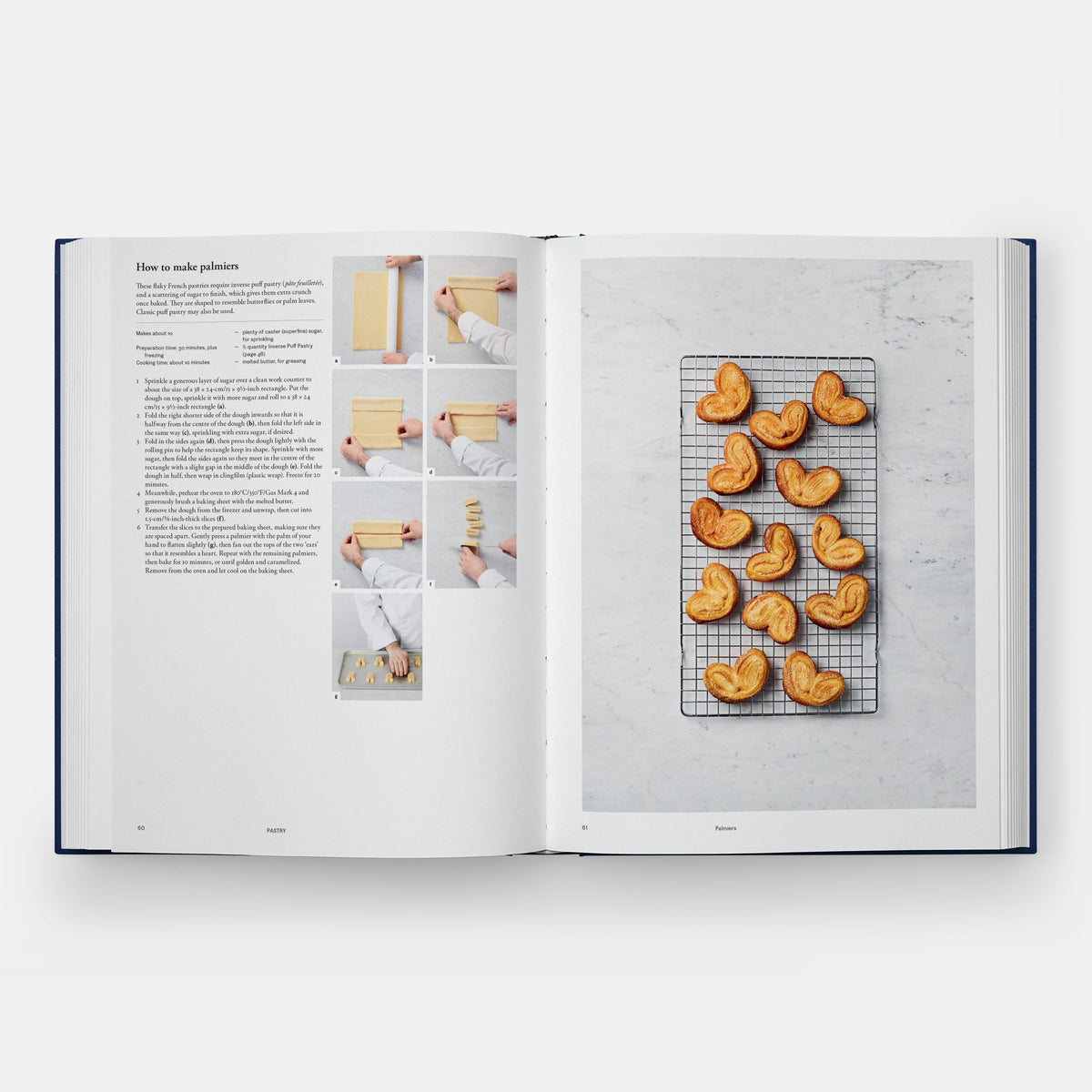 An open cookbook spread showing a recipe page on the left with text and small step-by-step photos, and a large photo of heart-shaped pastries on a cooling rack on the right, photographed on a light gray background.