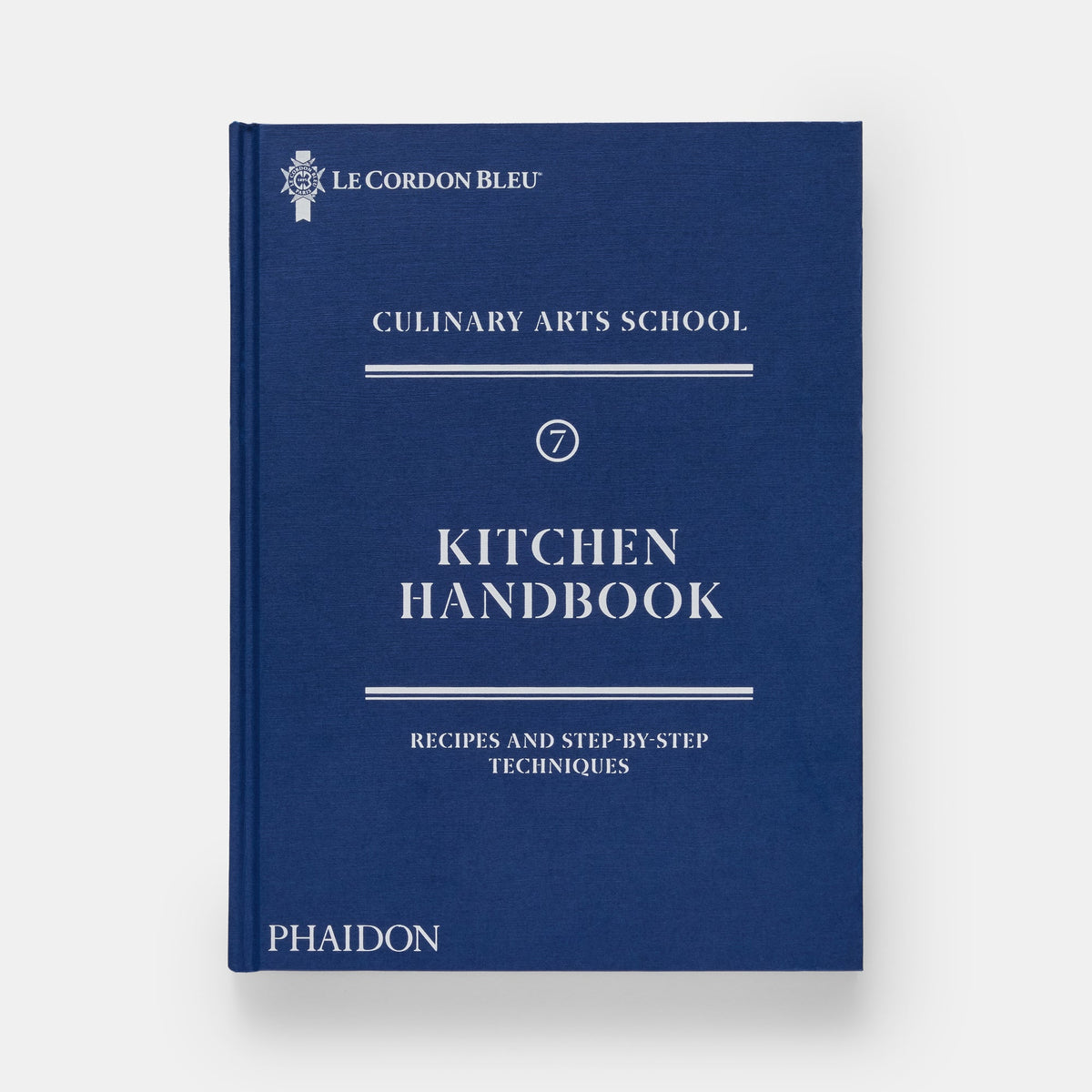 A hardcover book titled 'Kitchen Handbook' from Le Cordon Bleu Culinary Arts School, published by Phaidon. The book cover is a deep navy blue with white text and decorative lines, set against a clean, light gray background.