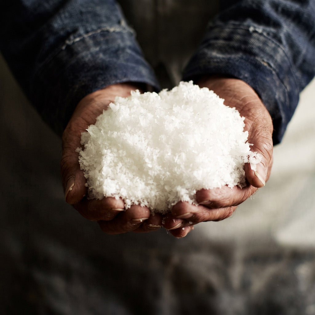A close-up of a person's hands holding a mound of Maldon coarse white salt crystals