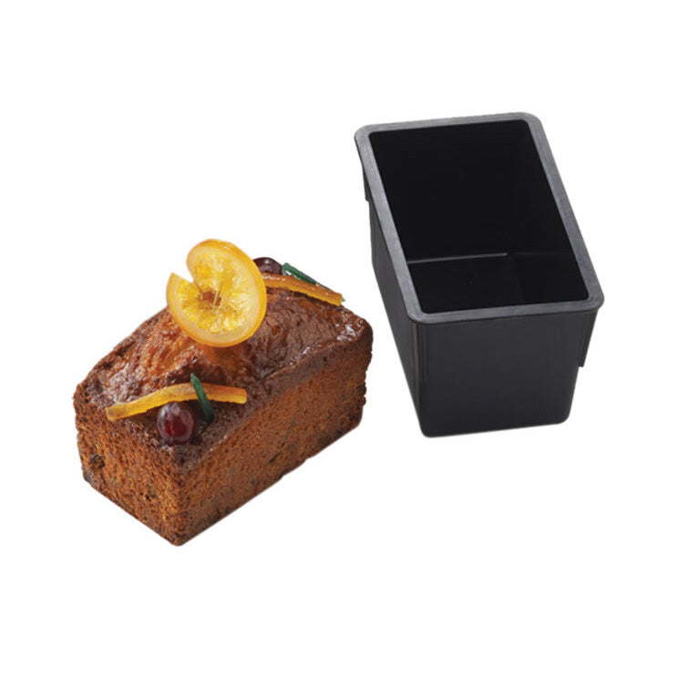 Black rectangular Matfer loaf cake pan next to a slice of fruitcake on a white background