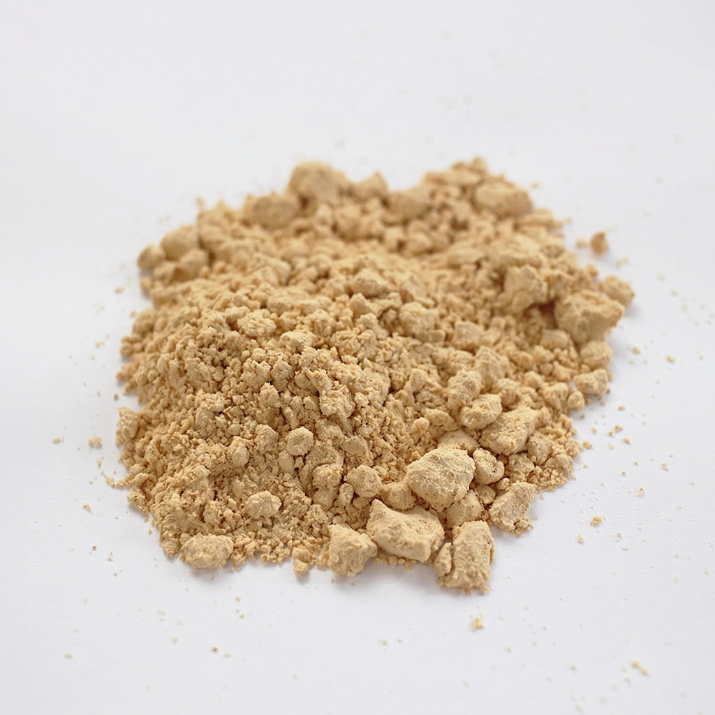 A small mound of light tan kinako powder or crumbly granules photographed on a plain white background.