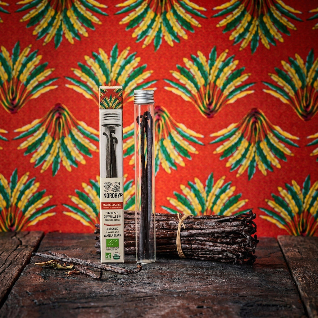 Norohy Organic Madagascar Bourbon Vanilla beans and packaging on a wooden surface with a colorful pineapple-patterned fabric background