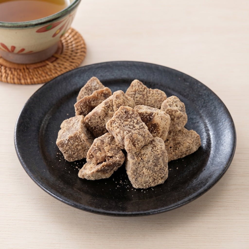 Dark plate with Okinawa Black Sugar in its rock form and a cup of tea on a light surface