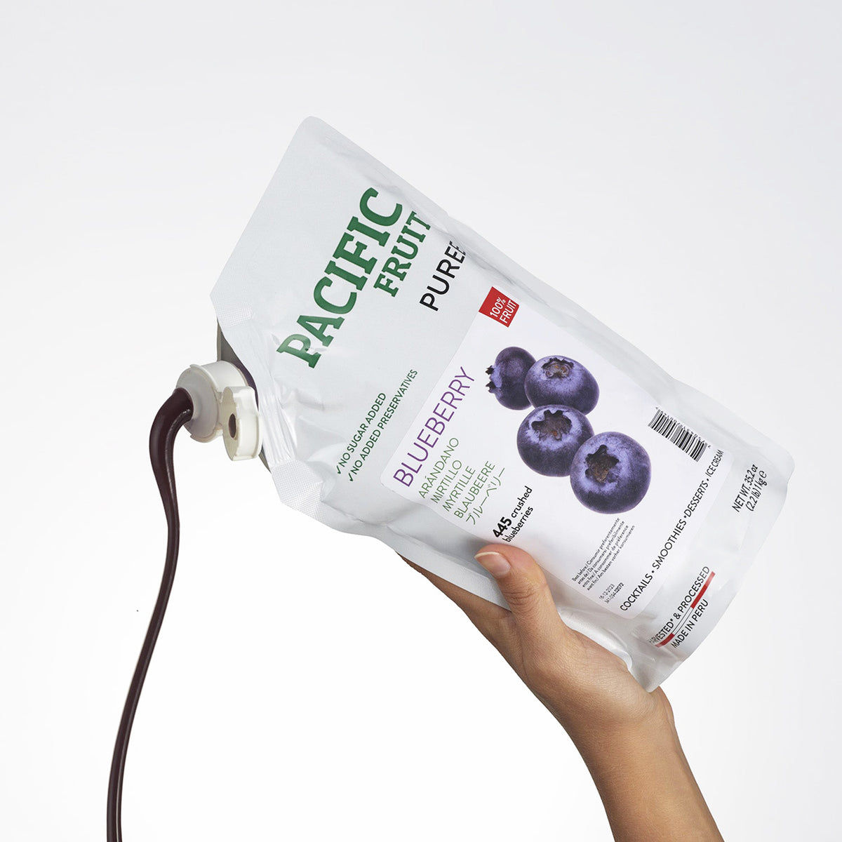 Hand holding a Pacific Fruit Puree Blueberry package with a white background