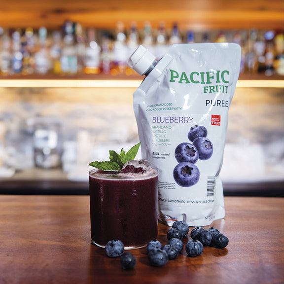 Pacific Fruit Blueberry Puree pouch with a blueberry mocktail and fresh blueberries on a bar counter.