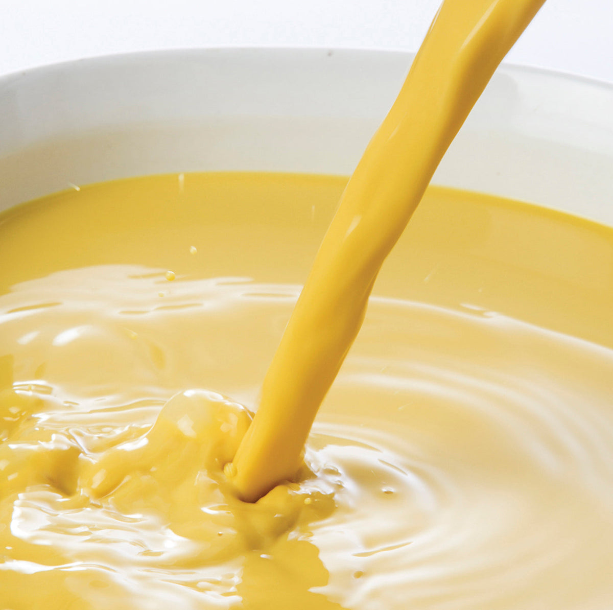 Yellow ginger puree juice being poured into a white bowl