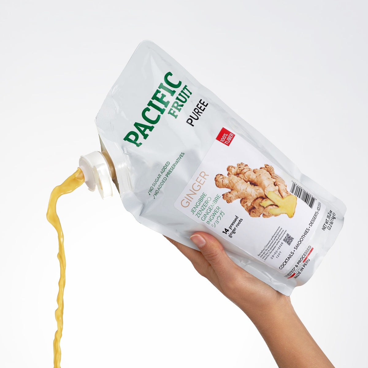 Hand holding a Pacific Fruit Ginger Puree pouch, pouring the puree onto a white background.