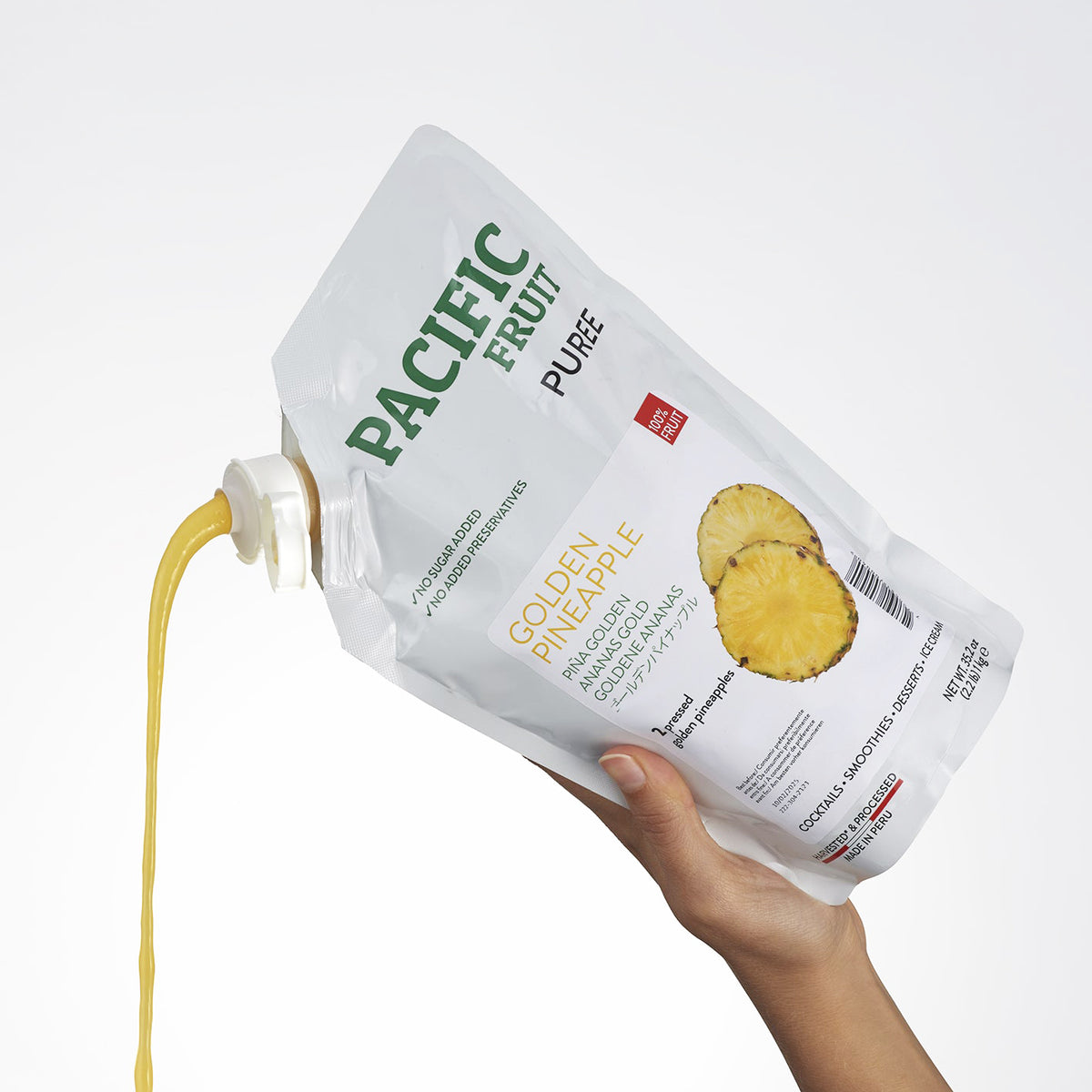 Hand holding a Pacific Fruit Puree Golden Pineapple pouch with juice spilling out on a white background