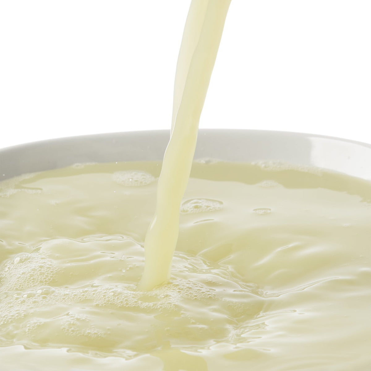 Lime puree juice being poured into a white bowl on a white background