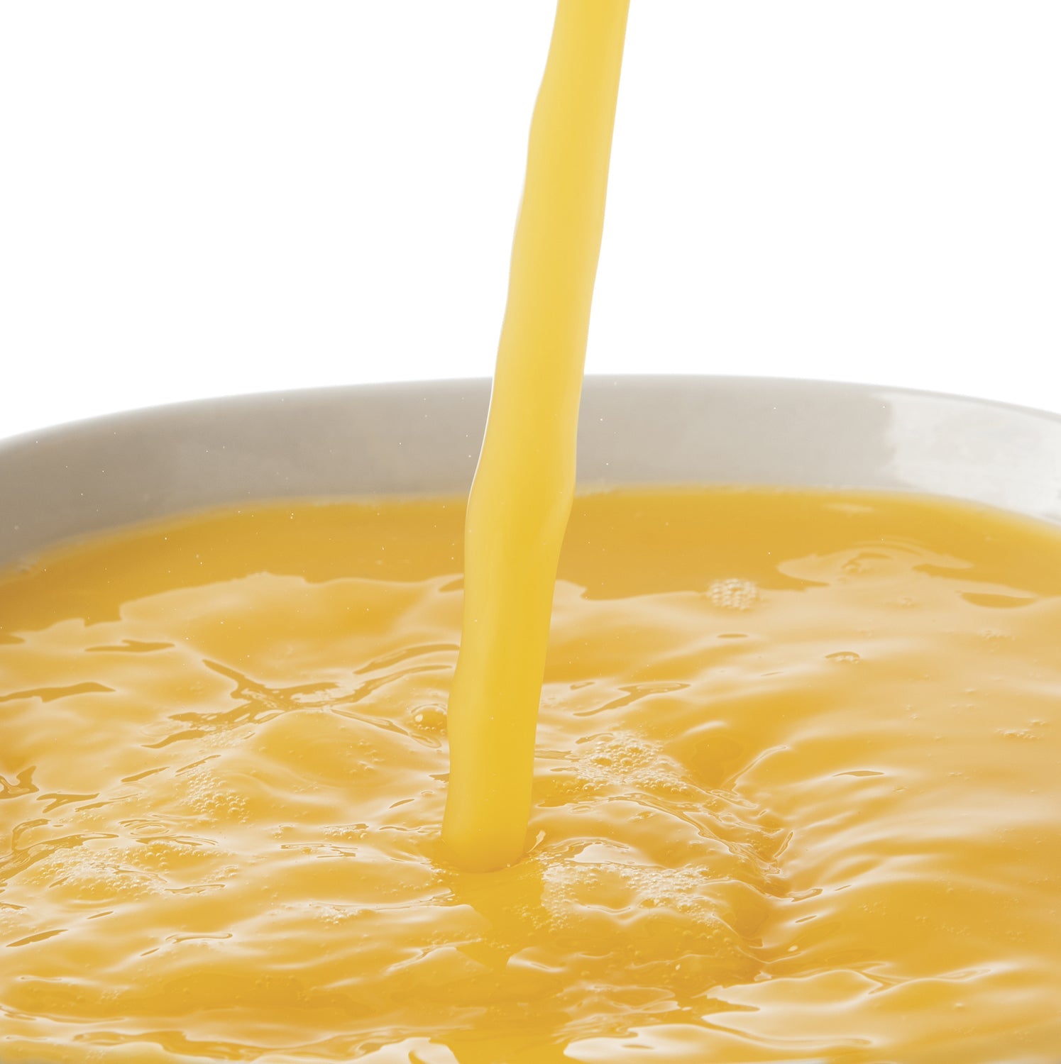 Orange puree juice being poured into a bowl on a white background