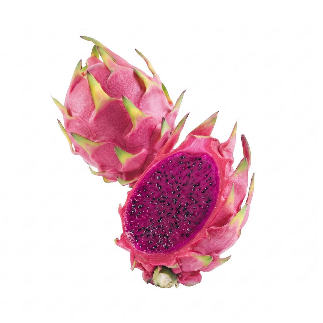 A whole and halved dragon fruit on a plain white background, showing the pink skin with green tips and a deep magenta-purple flesh filled with small black seeds.
