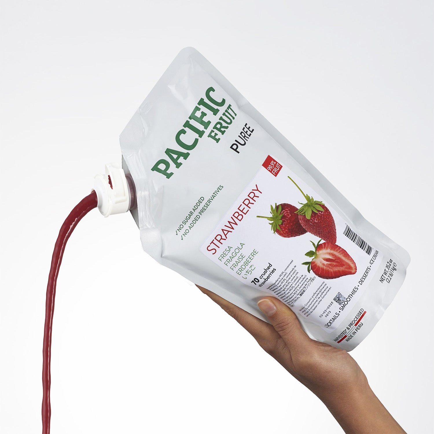 Hand holding a Pacific Fruit Puree strawberry pouch with a white background