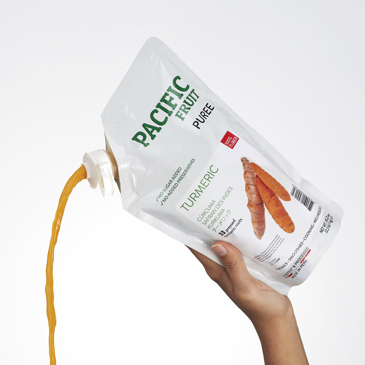 Hand holding a Pacific Fruit Puree Turmeric pouch with visible juice flow.