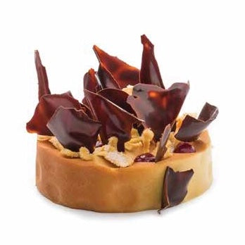 A small round pastry or tart with a golden-brown base, topped with glossy dark chocolate shards, nuts, and a few red berries, isolated on a white background.