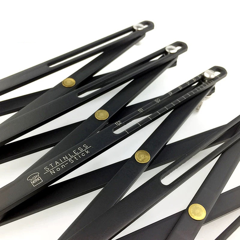 Four black stainless steel folding measuring sticks with gold-colored rivets and a non-stick coating, arranged diagonally on a white background.