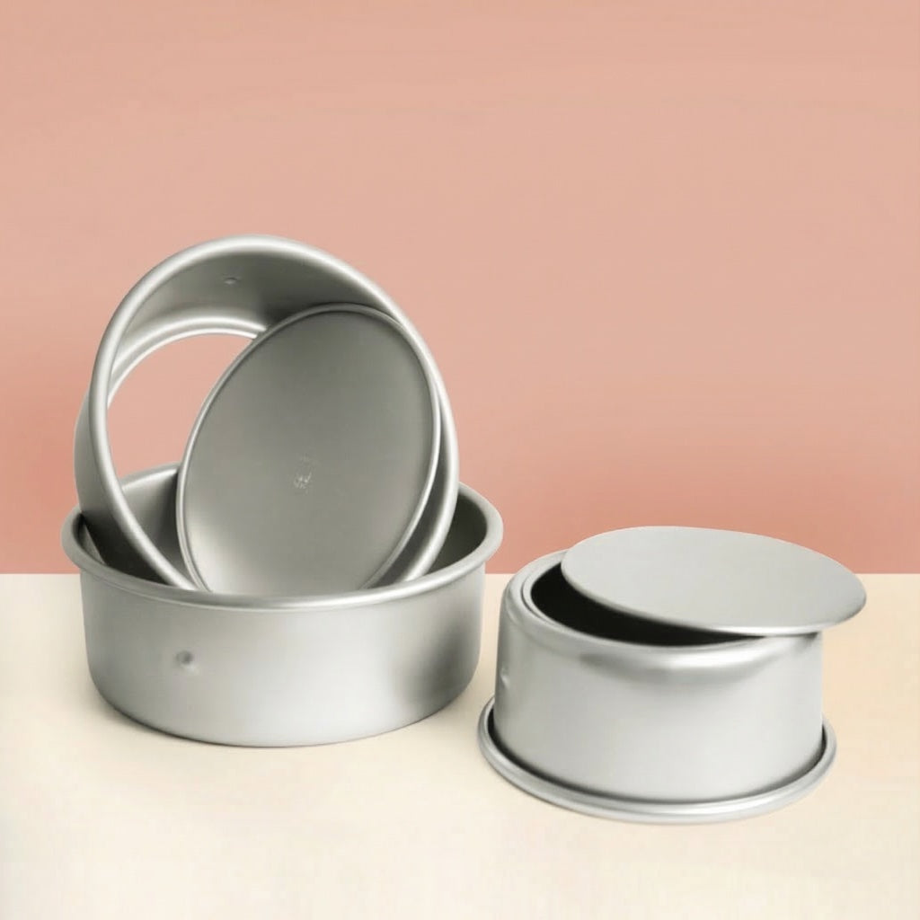Set of Sanneng Anodized Deep Round Cake Pans with removable bottom on a beige surface with a pink background
