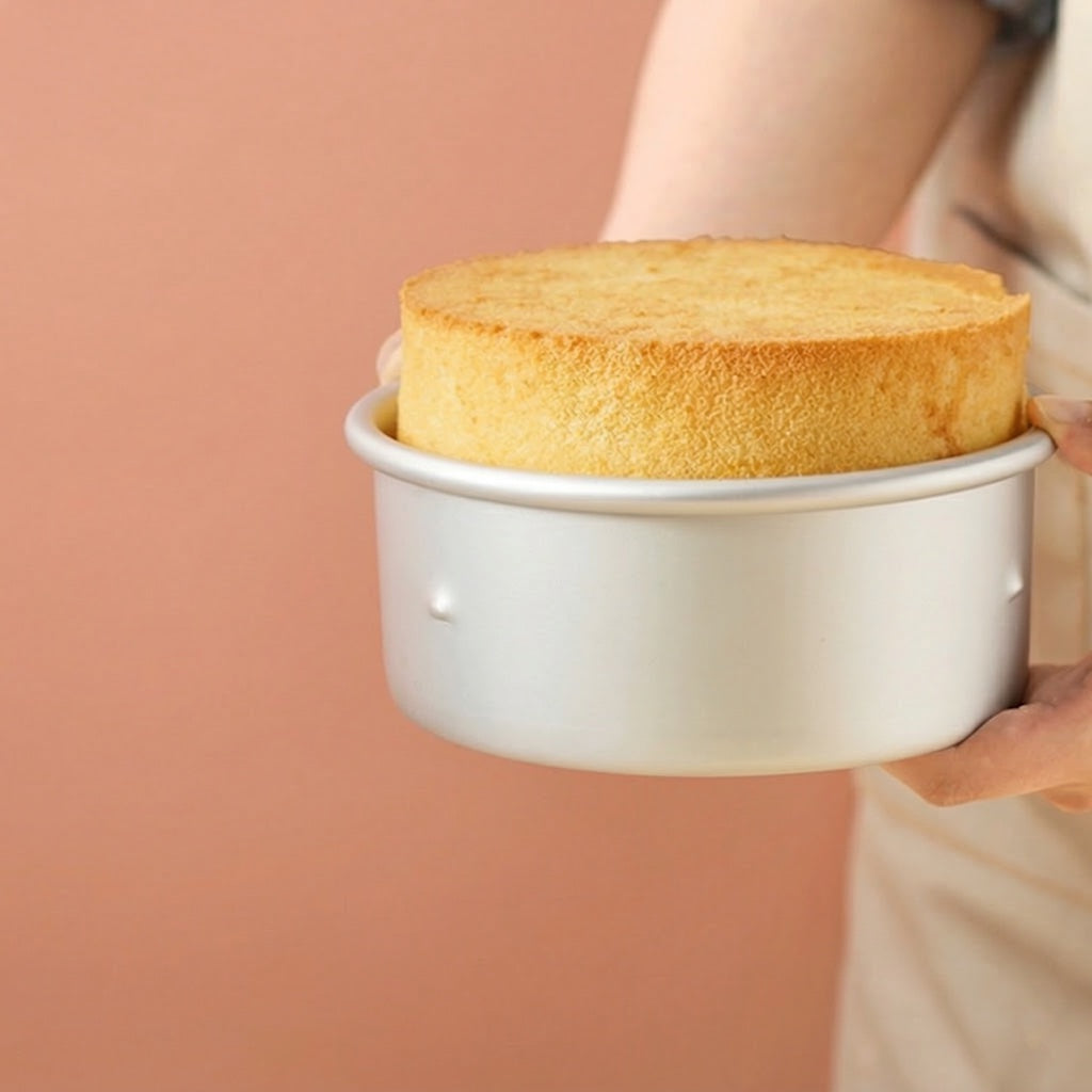 Person holding a round cake using Sanneng Anodized Deep Round Cake Pan with removable bottom against a pink background