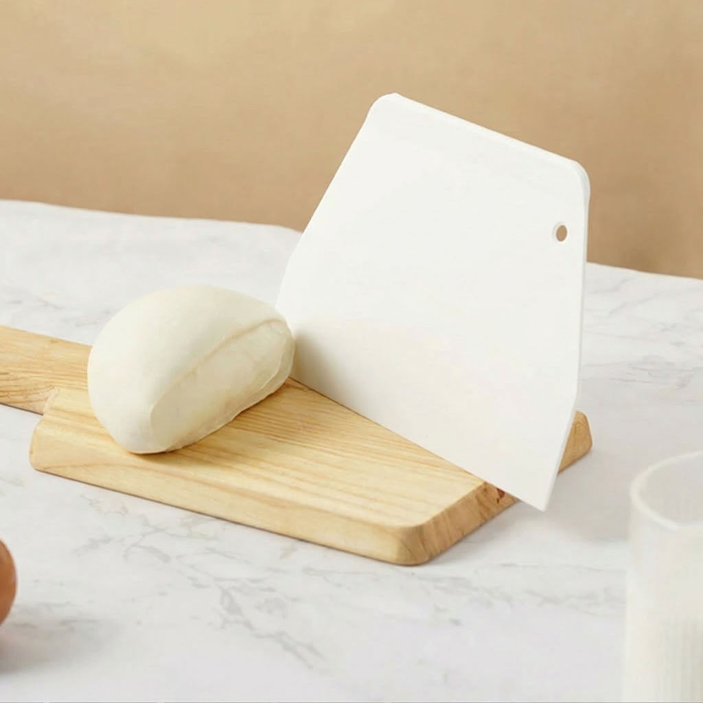 White SN4051 Sanneng scraper on a wooden cutting board with a ball of dough against a beige background