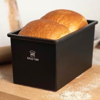 Two loaves of bread in a black loaf pan SN2196 on a wooden surface.