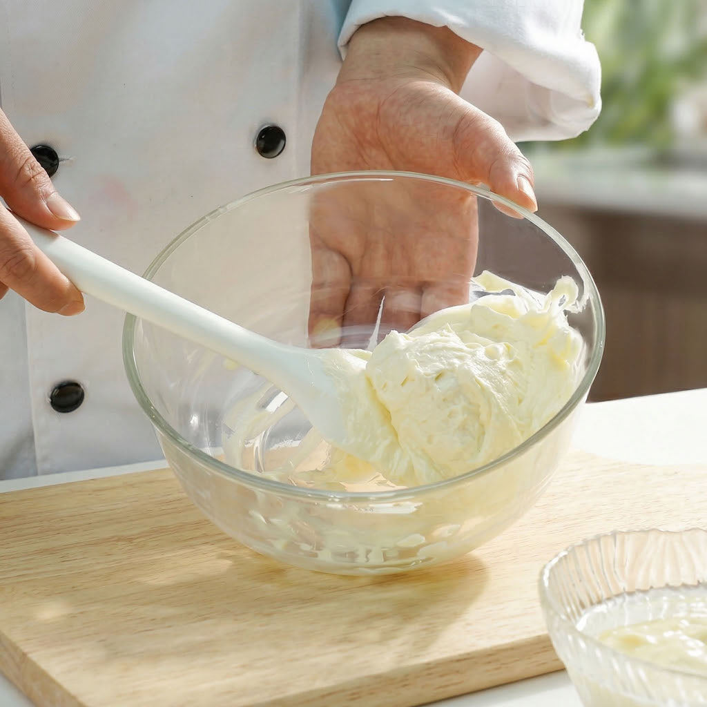 Person mixing ingredients in a glass bowl with a Sanneng white heat-resistant silicone spatula on a wooden surface.