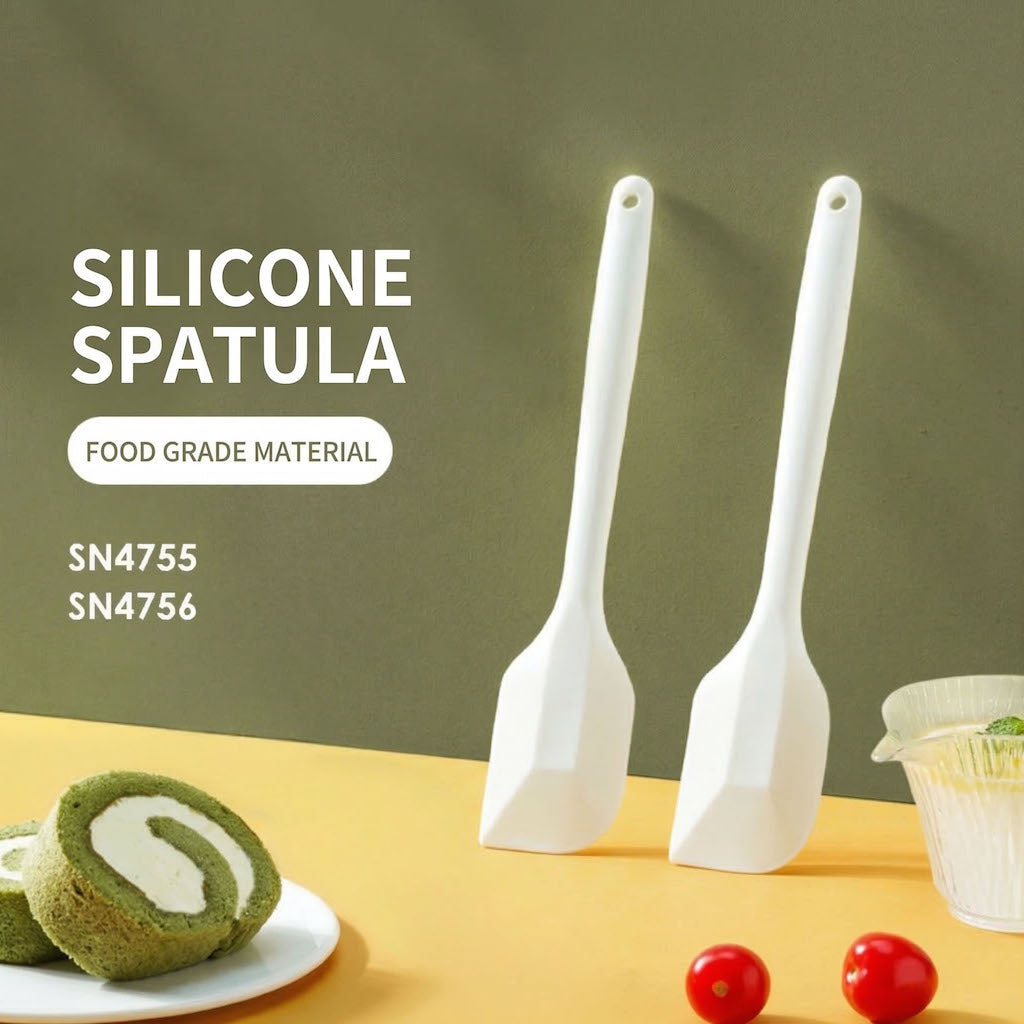 Two Sanneng white heat-resistant silicone spatulas on a yellow surface with food items and a green background.