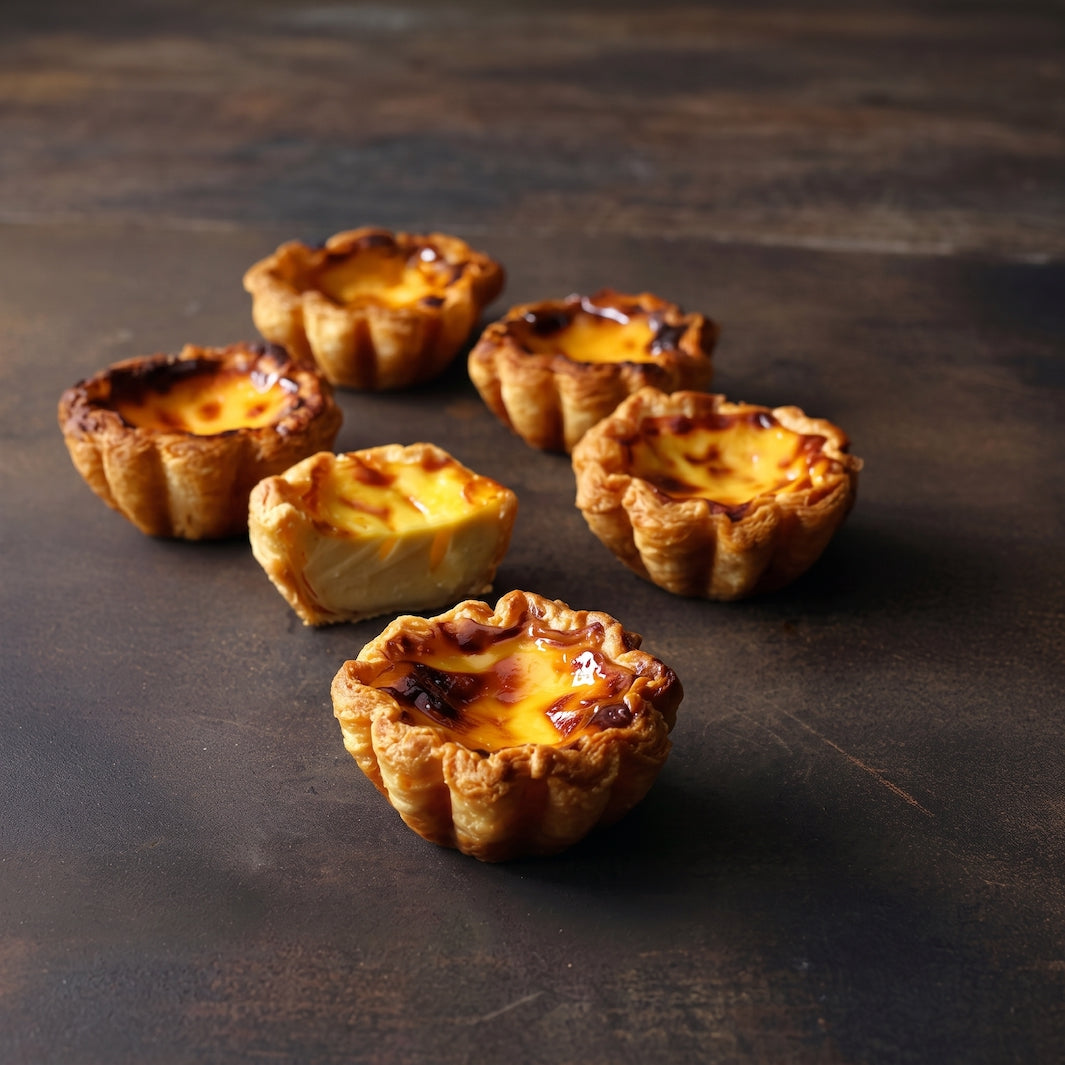 Five mini Portuguese custard tarts with golden-brown pastry shells and glossy caramelized egg tops, arranged on a dark rustic wooden surface.
